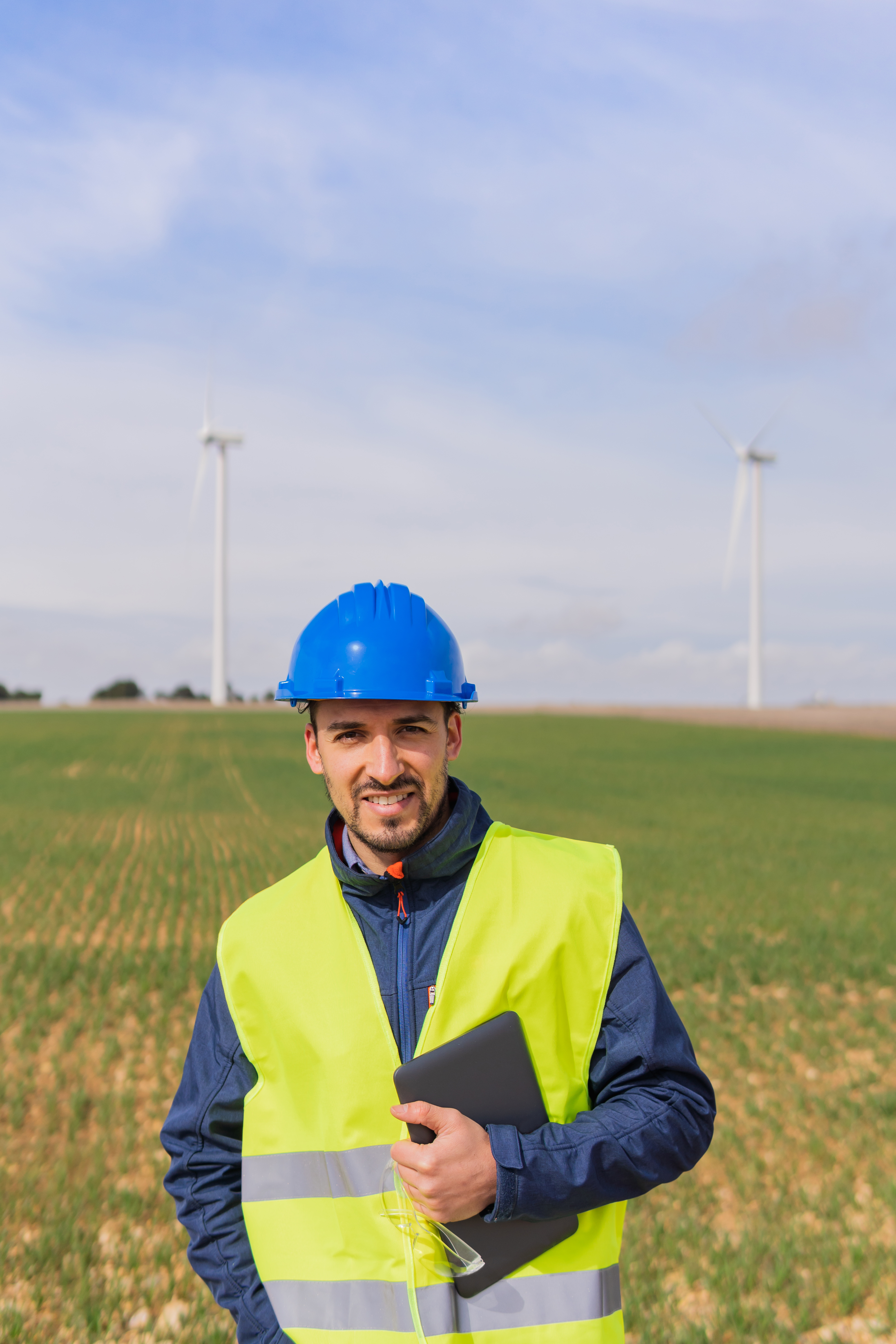 Positive male engineer in hardhat with tablet in hand looking at camera while standing on agricultural field in countryside on summer day